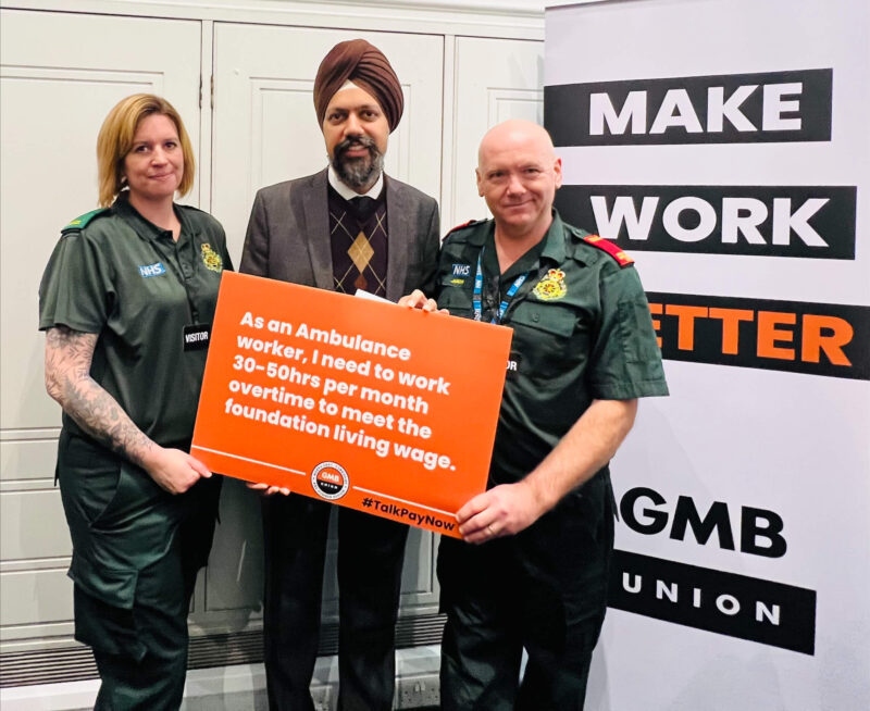 Tan Dhesi MP pictured holding a sign which reads: "As an Ambulance worker, I need to work 30-50hrs per month overtime to meet the foundation living wage".